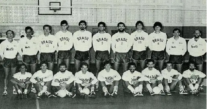 Equipe de vôlei masculino em ginásio, uniformes brancos com "Brasil".