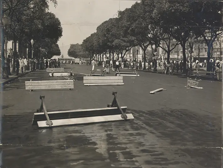 Motim em praça com barreiras de madeira e pessoas em movimento.