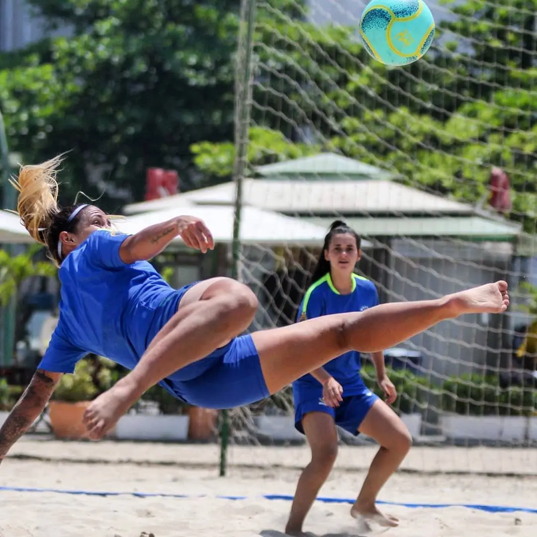 Jogadoras em ação durante partida de futebol de areia.