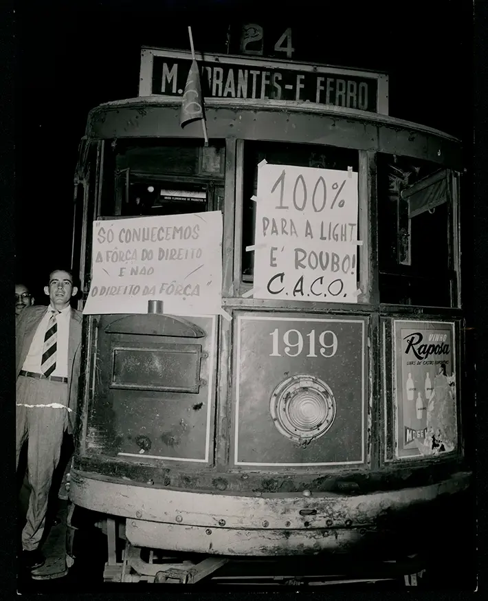 Fotografia preto e branco de bonde antigo com pessoas e panfletos.