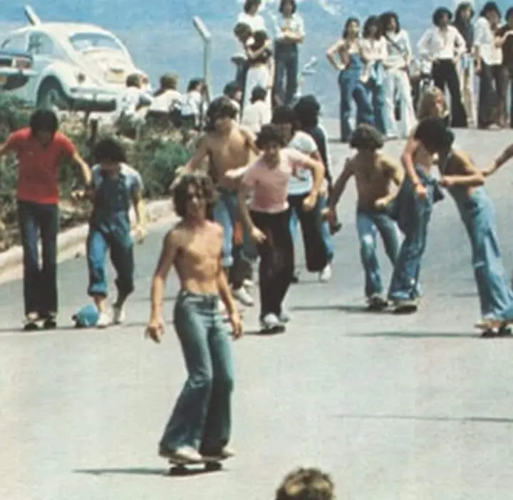Grupo de pessoas em rua, com carros e skatistas.