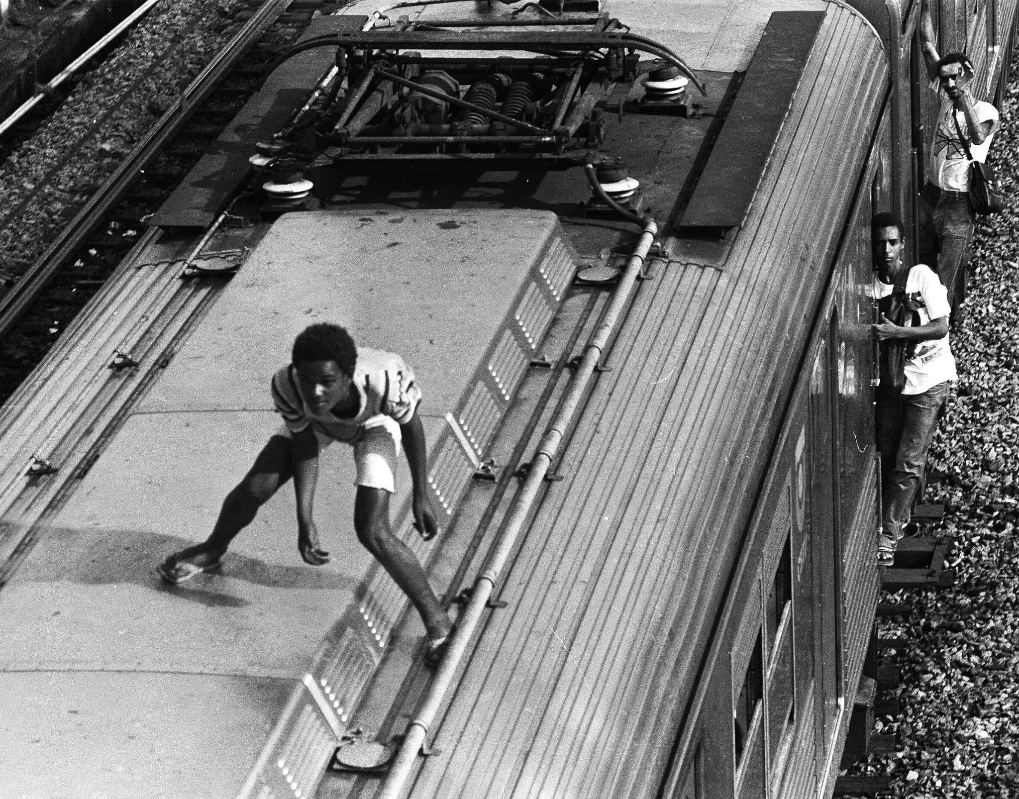 Dois homens em um trem: um caminhando sobre o teto, outro olhando pela janela.