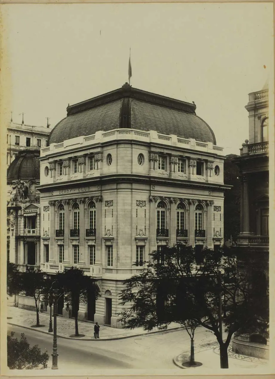 Edifício clássico com detalhes ornamentais e árvores em primeiro plano.