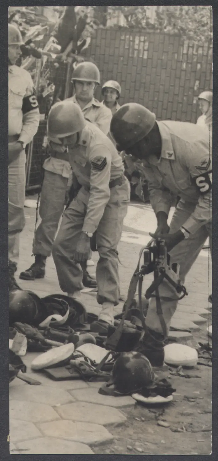 Grupo de militares em uniforme, equipamentos de proteção e cerca de madeira ao fundo.