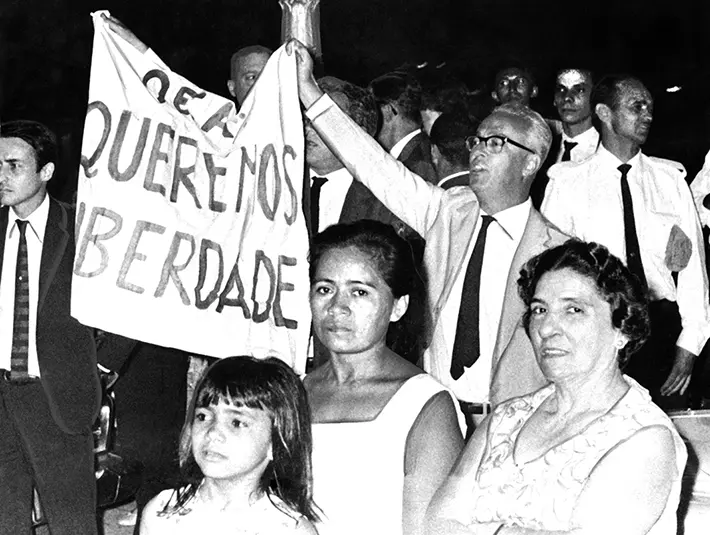 Três mulheres e uma criança protestam em praça, pedindo liberdade.