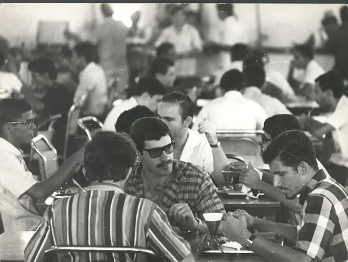 Grupo de pessoas reunidos em reunião ou café, conversando e interagindo.