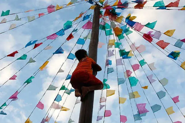 Festa junina com criança escalando poste colorido.