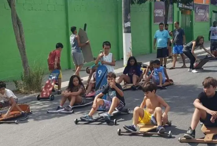 Crianças brincando com carrinhos de rolimã em uma rua verde.