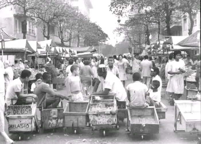 Feira livre com carrinhos de rolimãs e pessoas caminhando.