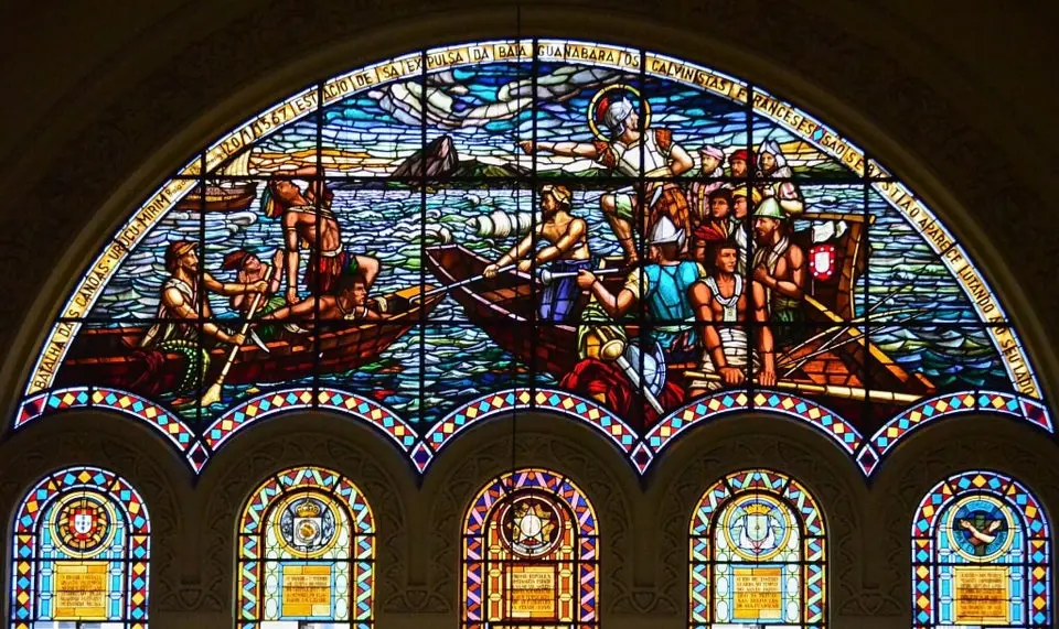 Vitral colorido em basílica, figuras em canoas e inscrições sobre Uruçumirim.