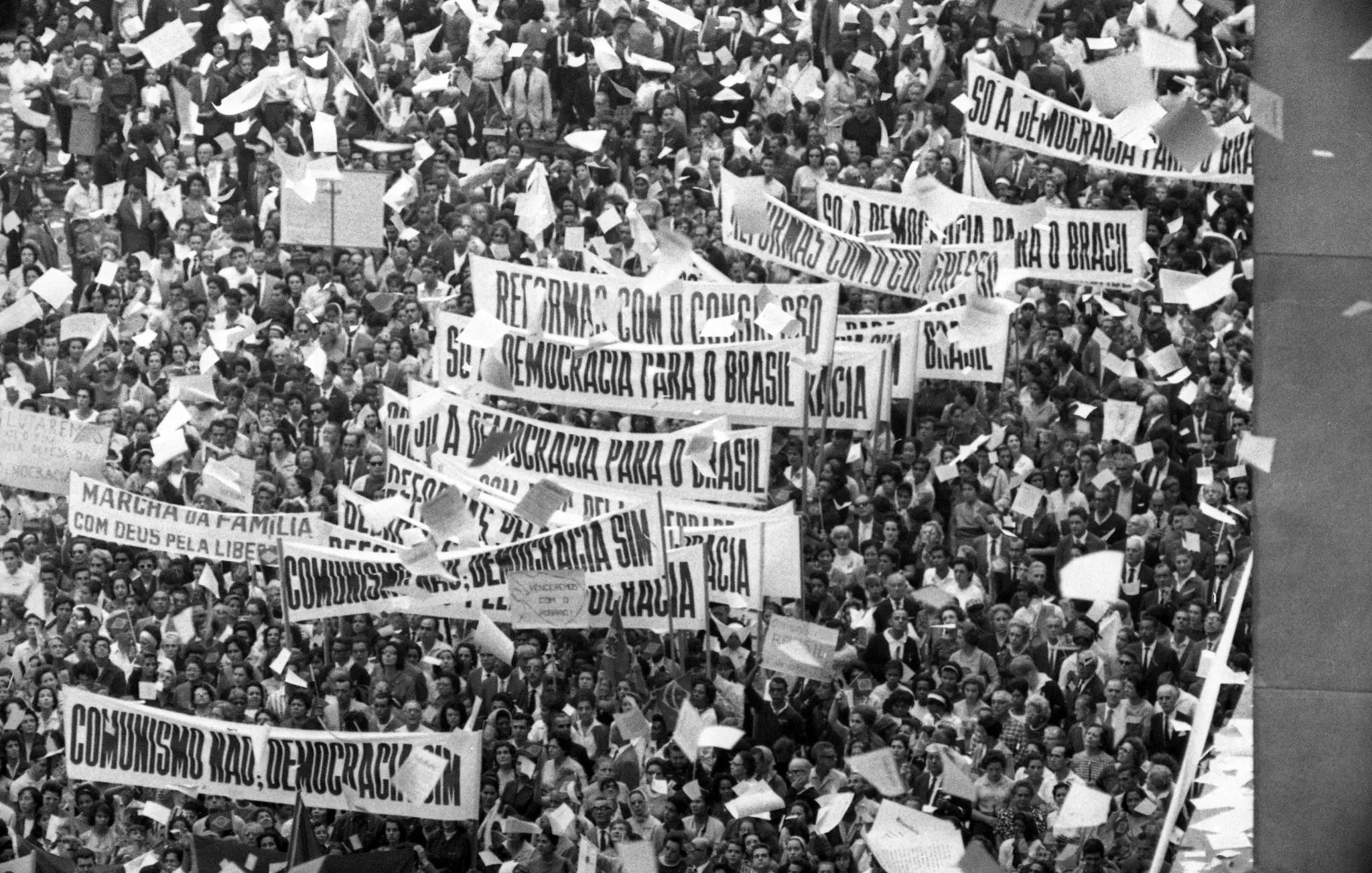 Manifestação em preto e branco com cartazes sobre democracia e reformas.