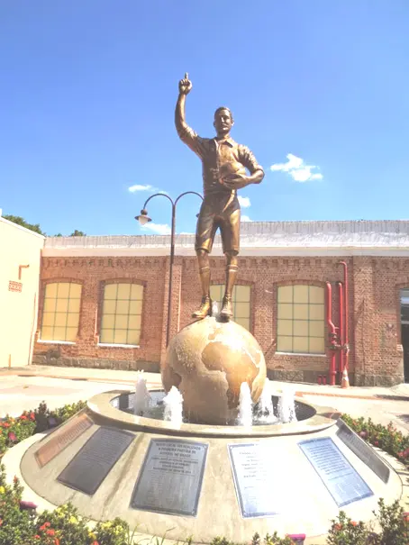Estátua de Thomas Donohoe em fonte, com farol à esquerda e construção histórica ao fundo.