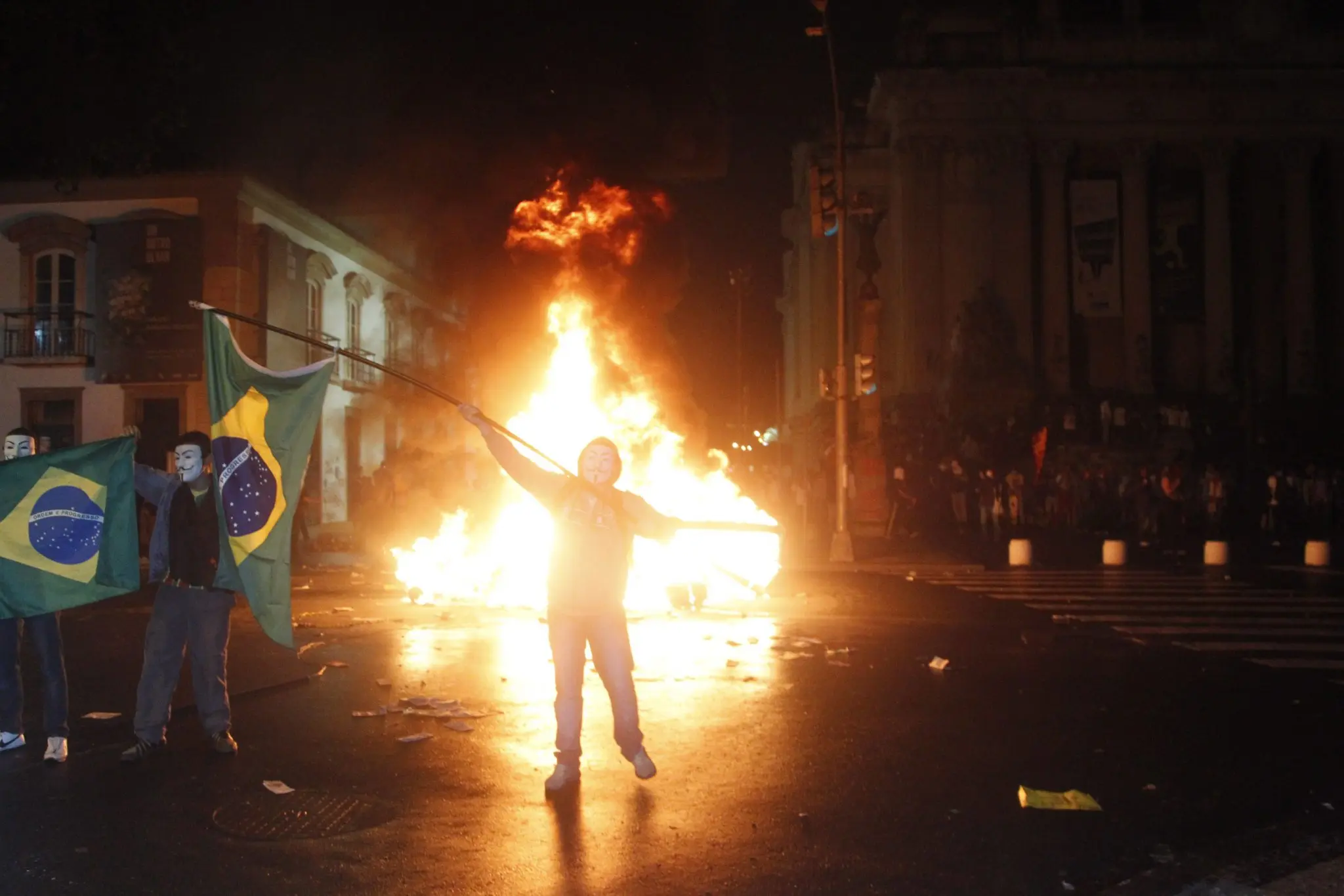 Manifestação noturna com bandeiras brasileiras e incêndio.