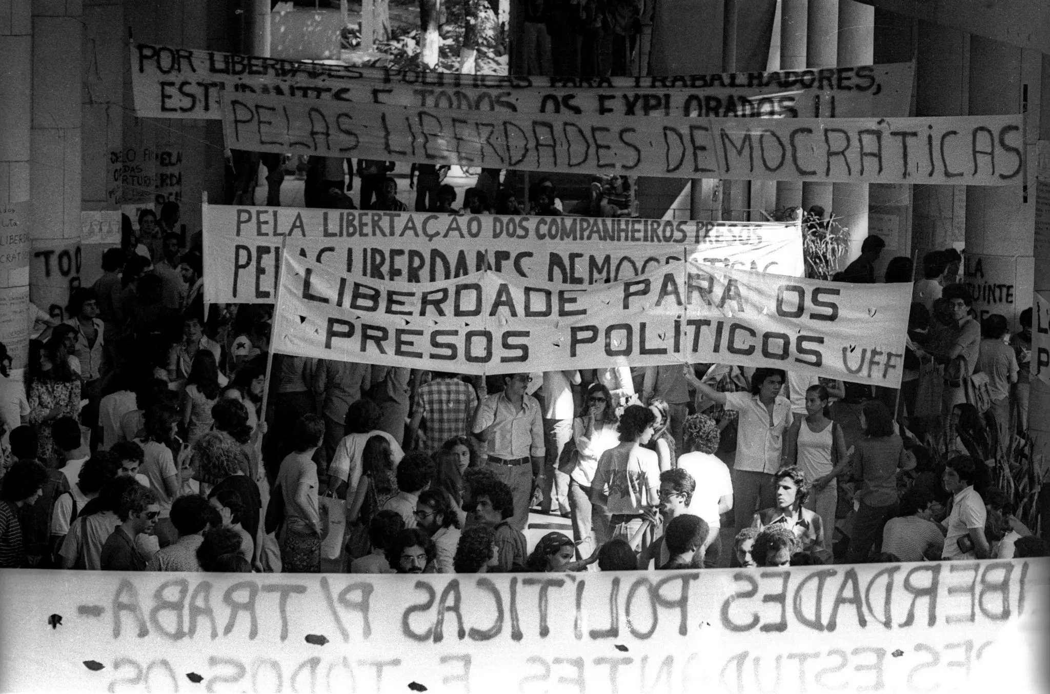 Manifestação estudantil com faixas e multidão em corredor e escada.