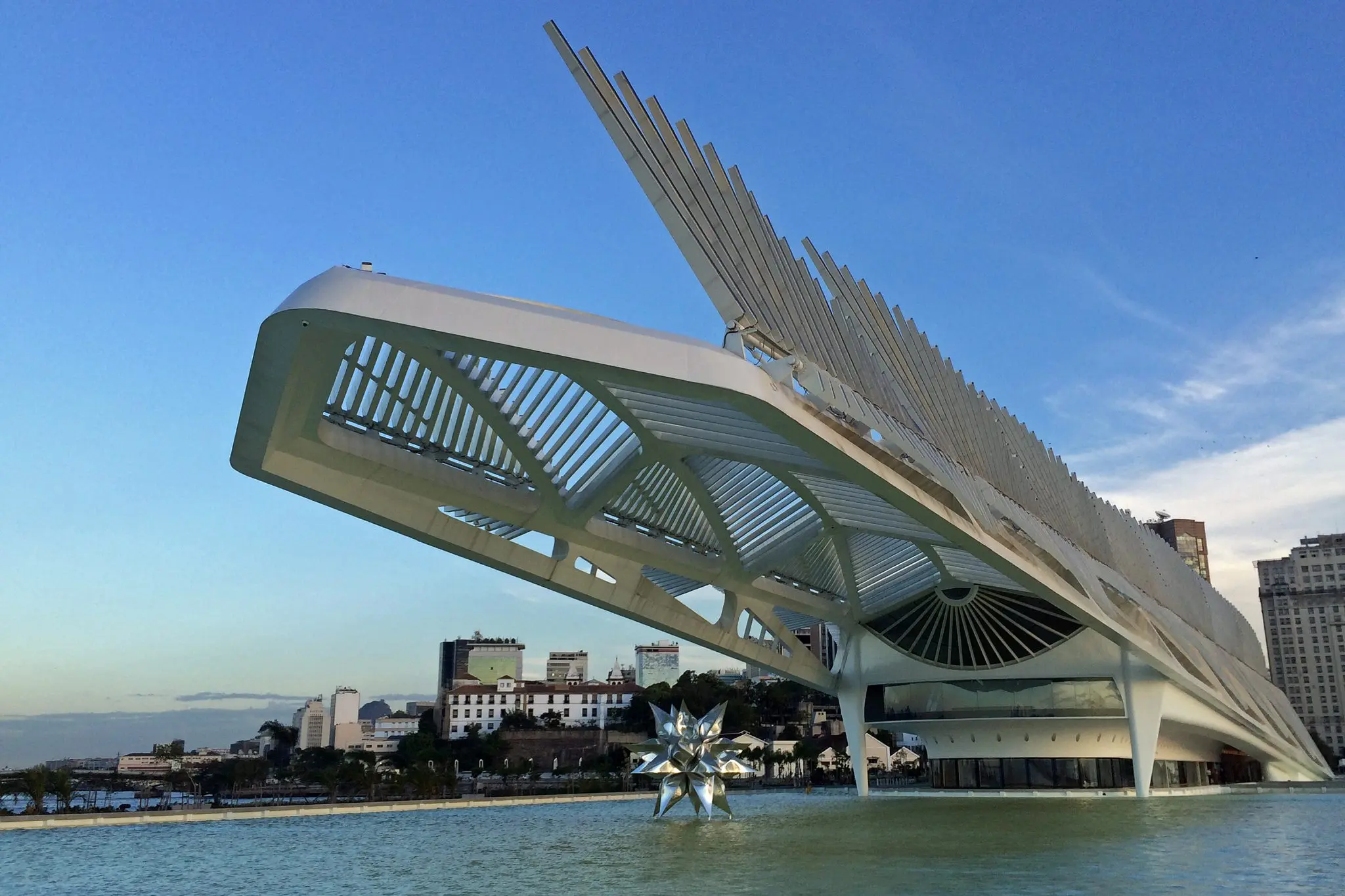 Edifício moderno em Porto Maravilha, Rio de Janeiro, com estrutura curvada e espelho d'água refletindo.