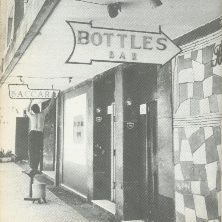 Estabelecimento "Bottles Bar" com entrada fechada e placa "Baccara" pendurada.