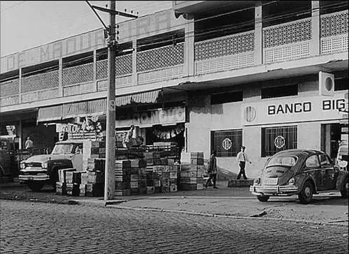 Rua comercial com carros antigos e pessoas caminhando.