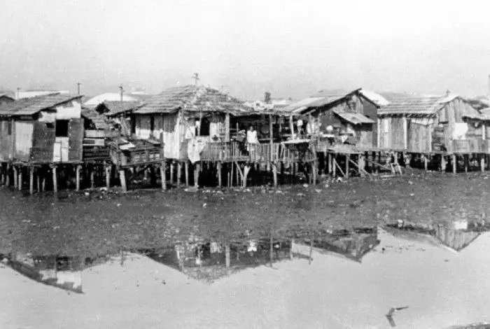 Casas em pilares sobre água, com telhados inclinados e roupas pendentes.