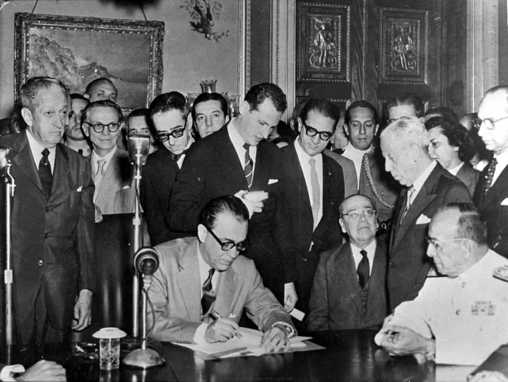 Reunião formal em preto e branco, assinatura de documentos.