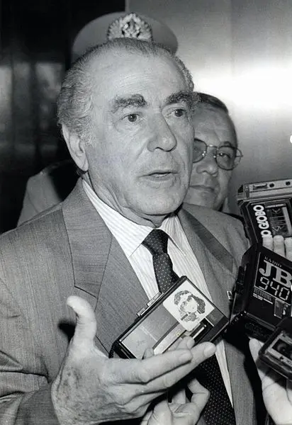 Homem falando com jornalistas em terno clássico.