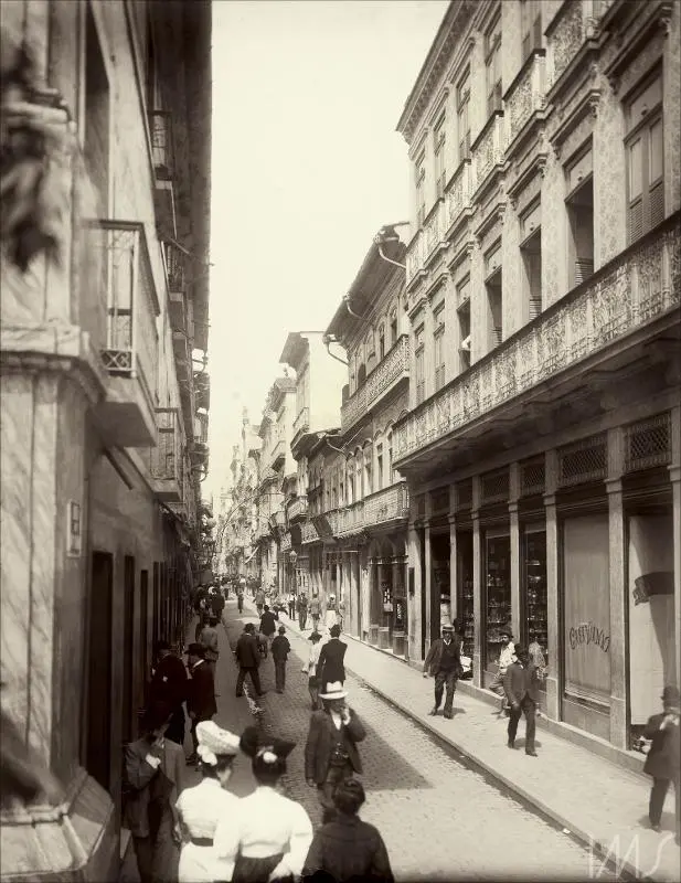 Uma rua urbana antiga com construções antigas e pessoas caminhando.