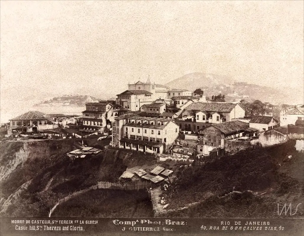 Cidade montanhosa com casas, igreja e colina em preto e branco.
