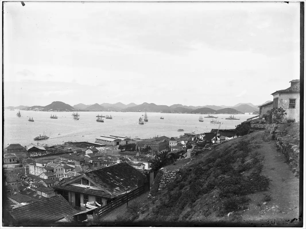Cidade costeira com navios e montanhas verdes.