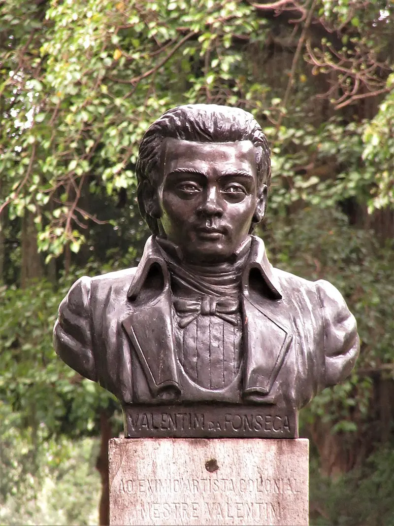 Estátua de bronze de homem em terno clássico em ambiente natural.