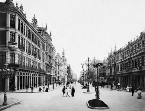 Edifícios clássicos e praça com árvores em avenida antiga.