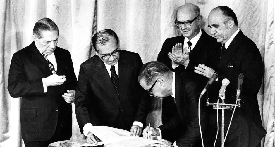 Cinco homens em trajes formais, meados do século XX, assinando documentos.