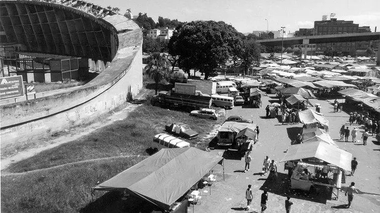 Mercado ao ar livre com barracas e viaduto.