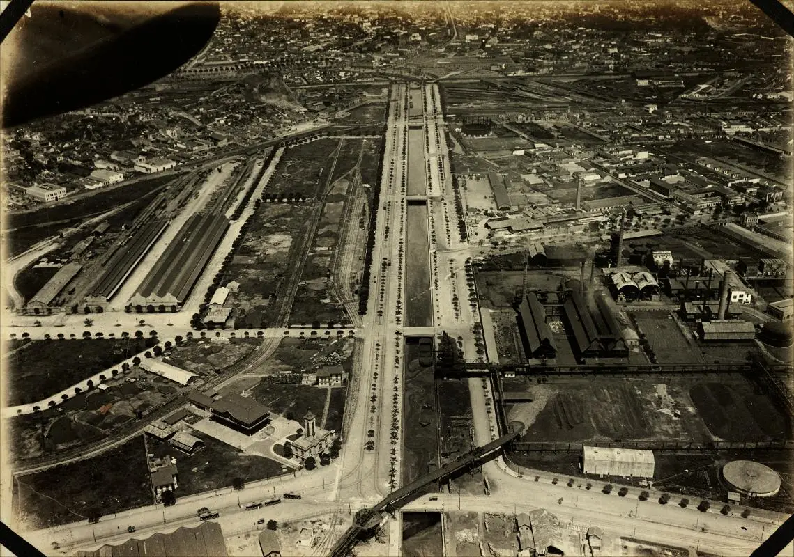 Imagem urbana com edifícios industriais, via férrea e áreas residenciais.