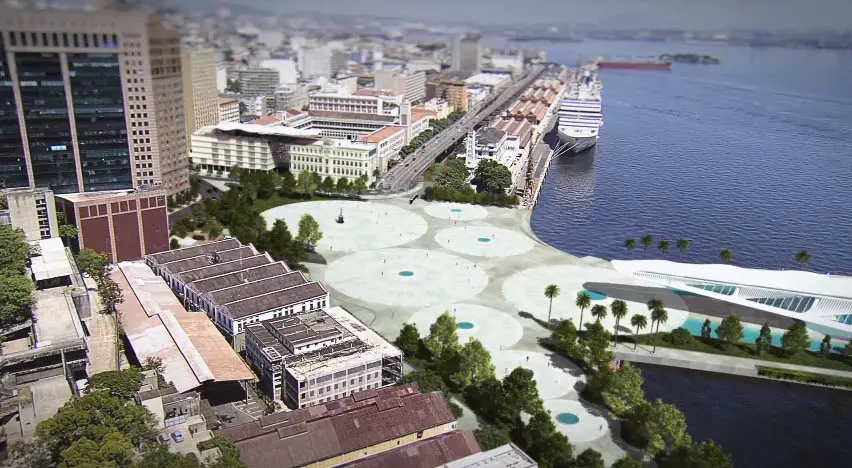 Cidade costeira com edifícios azuis, complexo arquitetônico, espaço aberto com círculos, árvores verdes, navio de cruzeiro e estrutura moderna.