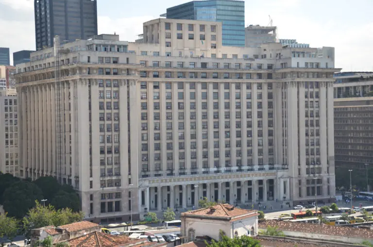 Edifício monumental com janelas horizontais, telhados vermelhos e céu parcialmente nublado.
