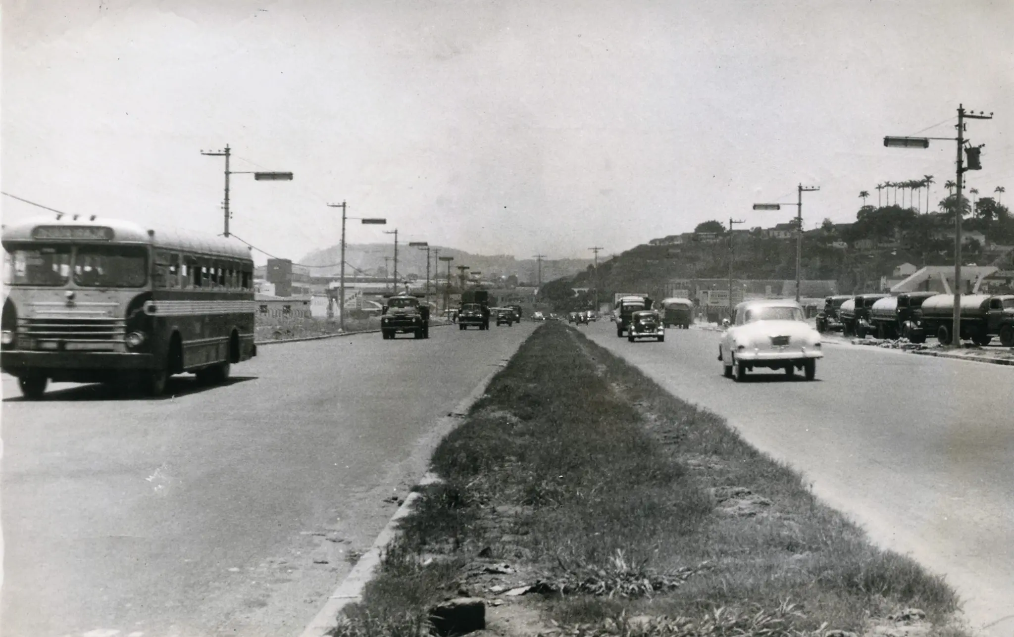 Estrada com tráfego, incluindo um ônibus antigo em movimento e vários veículos circulando.