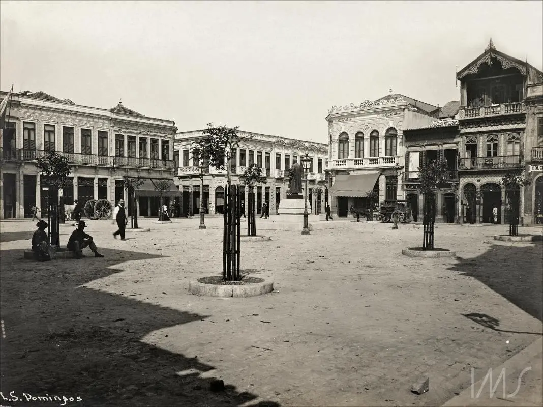 Praça histórica com edifícios ornamentados e estátua central.