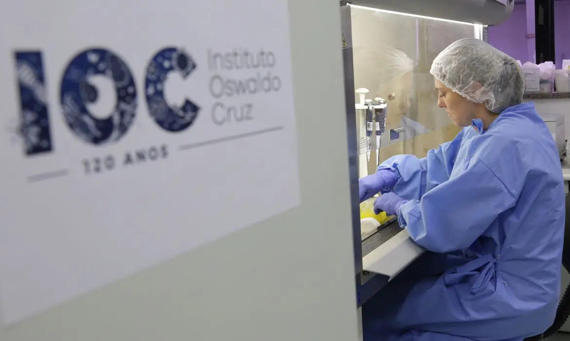 Laboratório com logotipo do IOC e pessoa trabalhando em equipamento.
