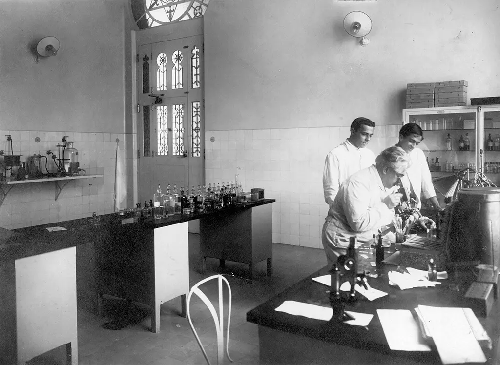 Laboratório científico com cientistas examinando microscópio.