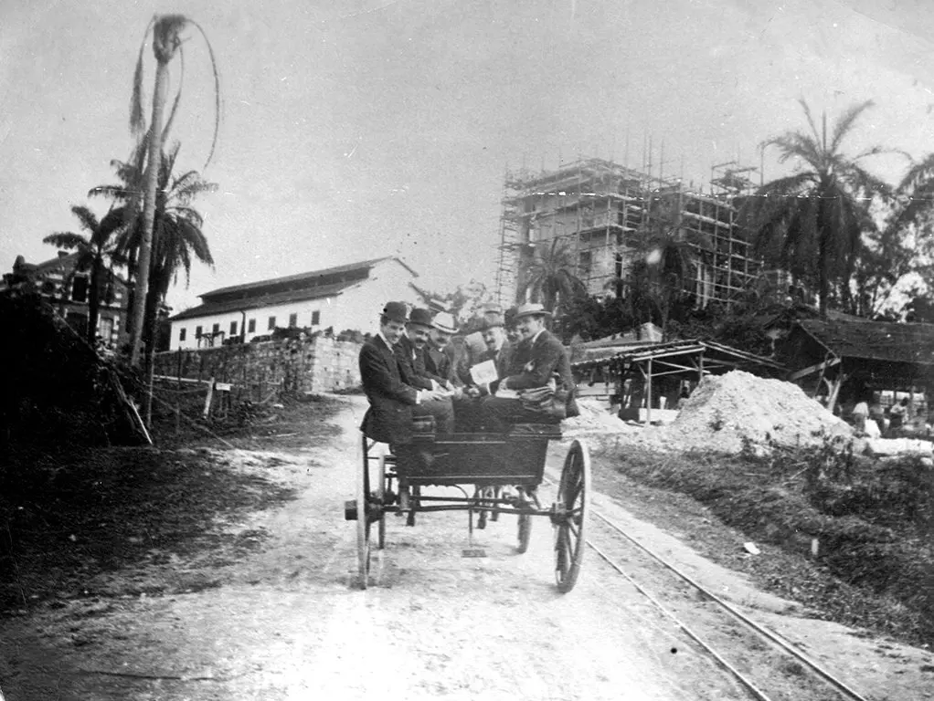 Imagem histórica em preto e branco com palmeira, carruagem e construções antigas.