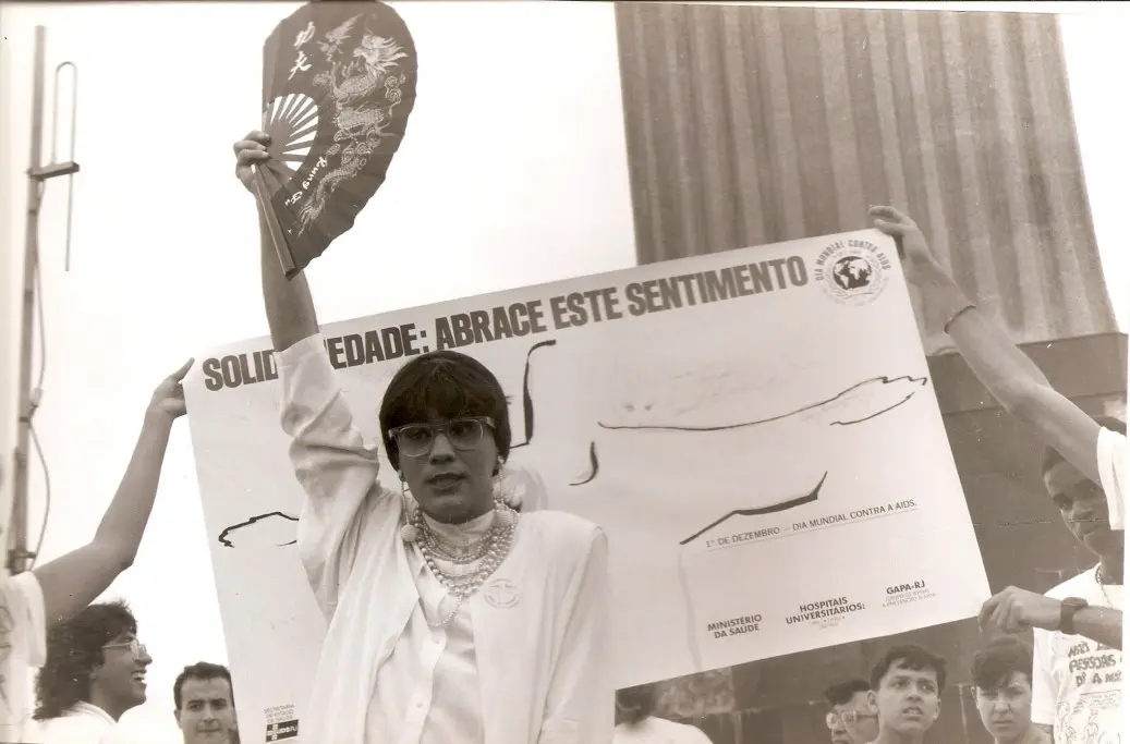 Manifestação contra a AIDS em preto e branco, com mulher segurando cartaz de solidariedade.