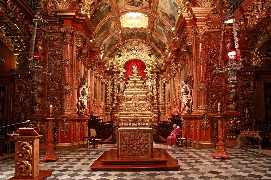 Interior de igreja barroco com decoração rica em madeira e azulejos xadrez.