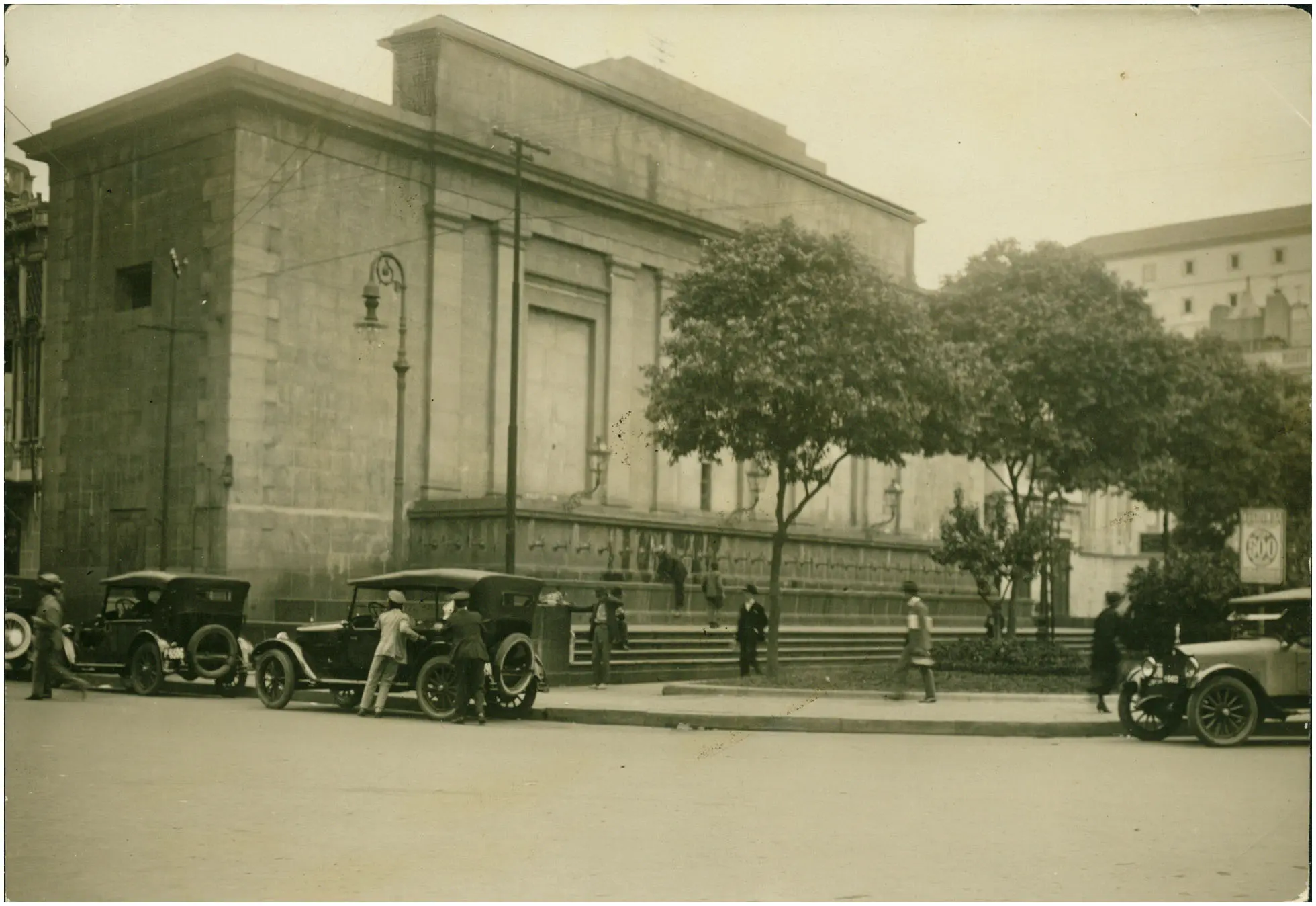 Edifício clássico com árvores e carros antigos em dia ensolarado.