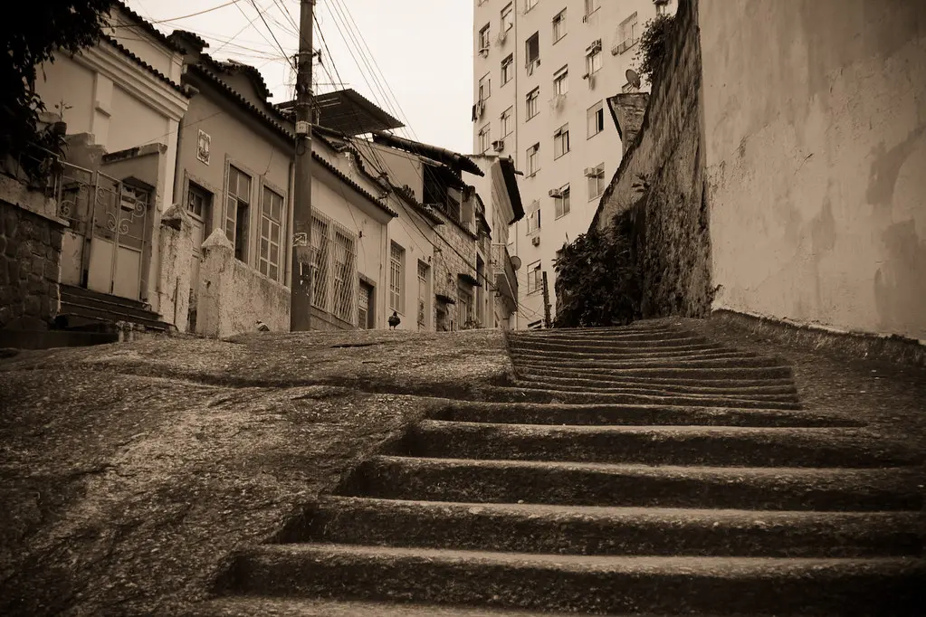 Uma rua em colina com casas antigas e prédio alto.