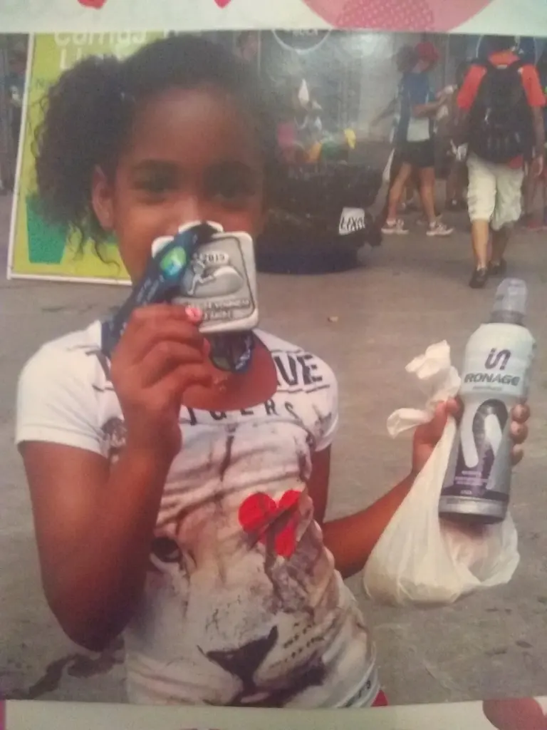 Menina sorridente com medalha e frasco de água.