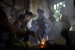 Grupo dançando em torno de fogueira, trajes tradicionais, luz natural.