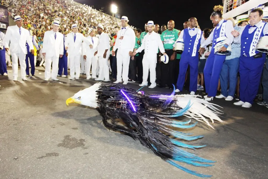 Escola de samba em desfile noturno com papagaio azul e branco.