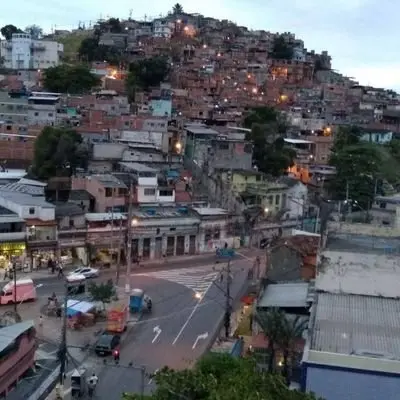 Área urbana durante o crepúsculo com edifícios coloridos, ruas e colina iluminada.