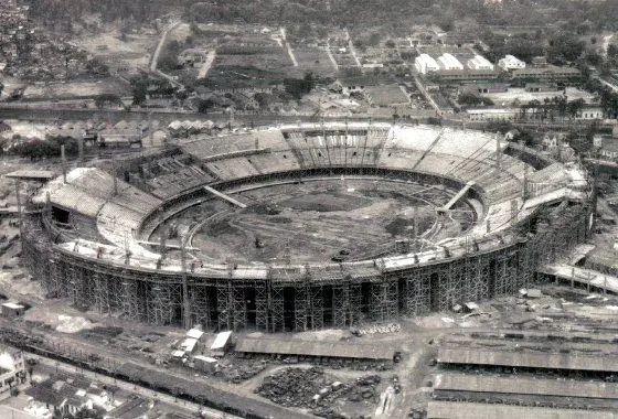 Estádio Maracanã em construção, com andaimes e edifícios ao redor.