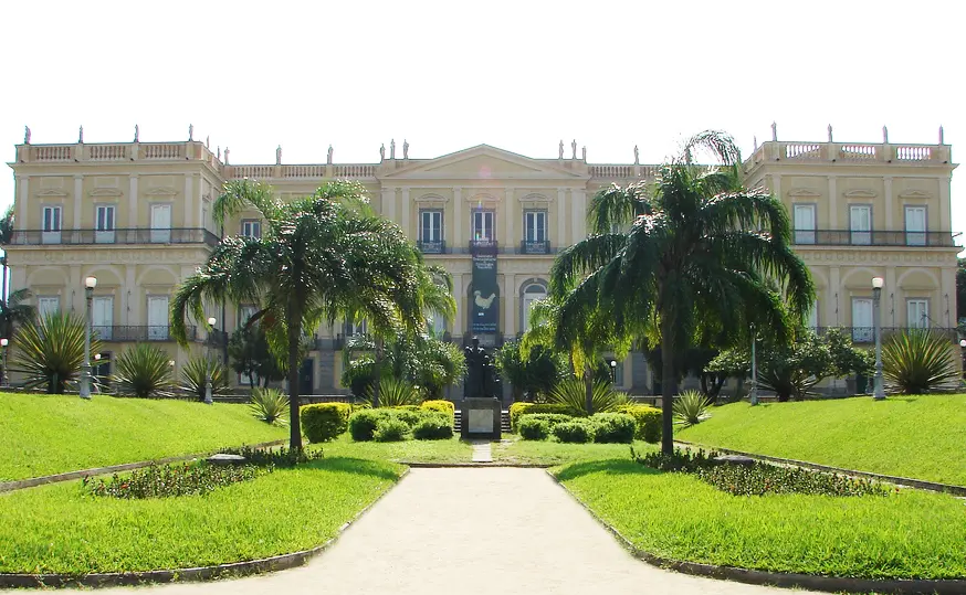 Palácio clássico com palmeiros e gramado bem cuidado.