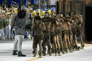 Dançarinos em trajes tradicionais formando uma linha reta durante uma apresentação de escola de samba.